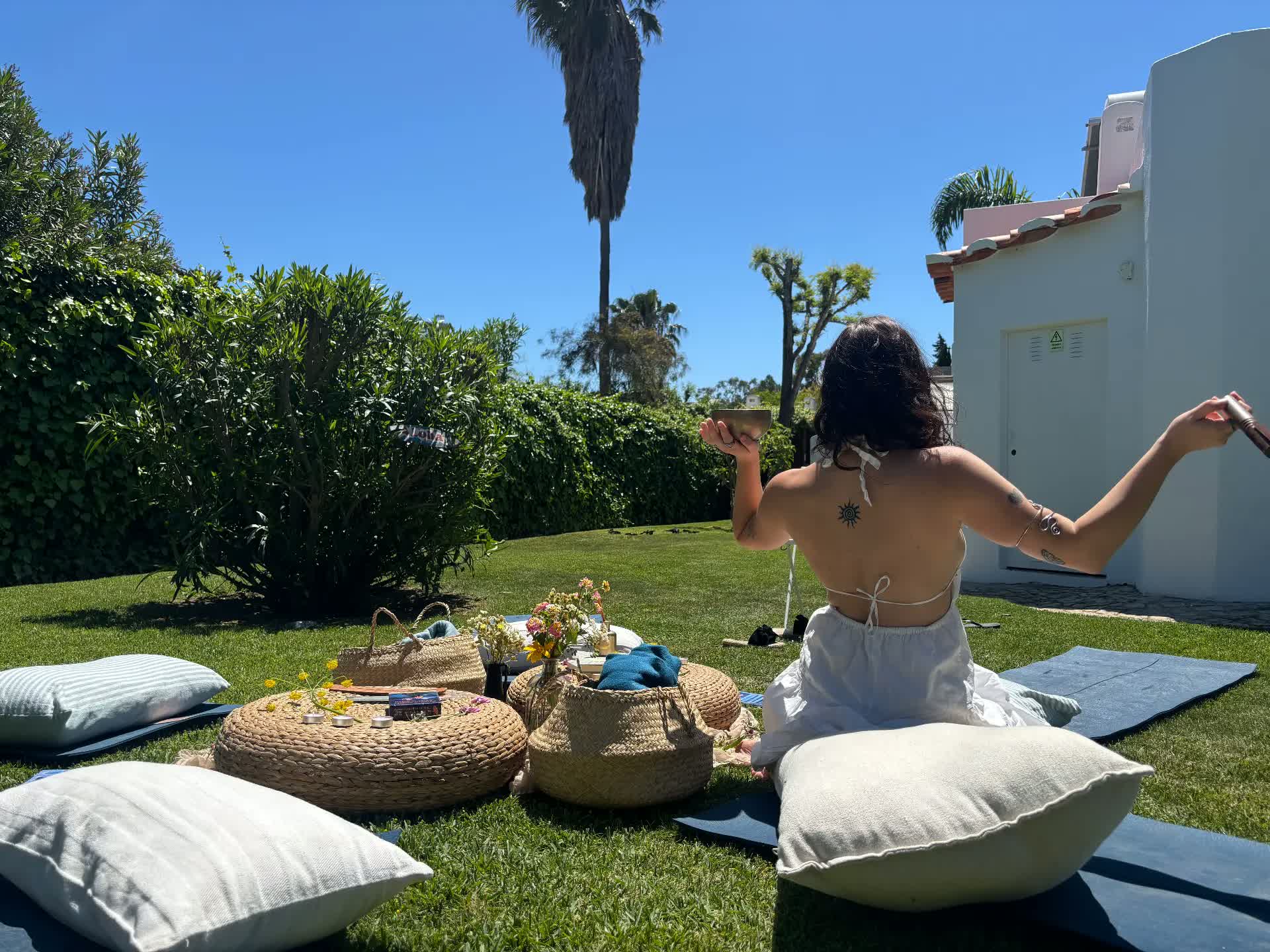 A woman in a white dress sitting in a garden holding a singing bowl
