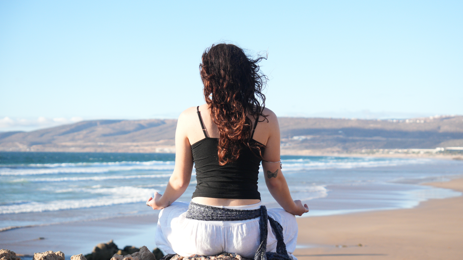 A woman meditating on a quiet beach at sunrise